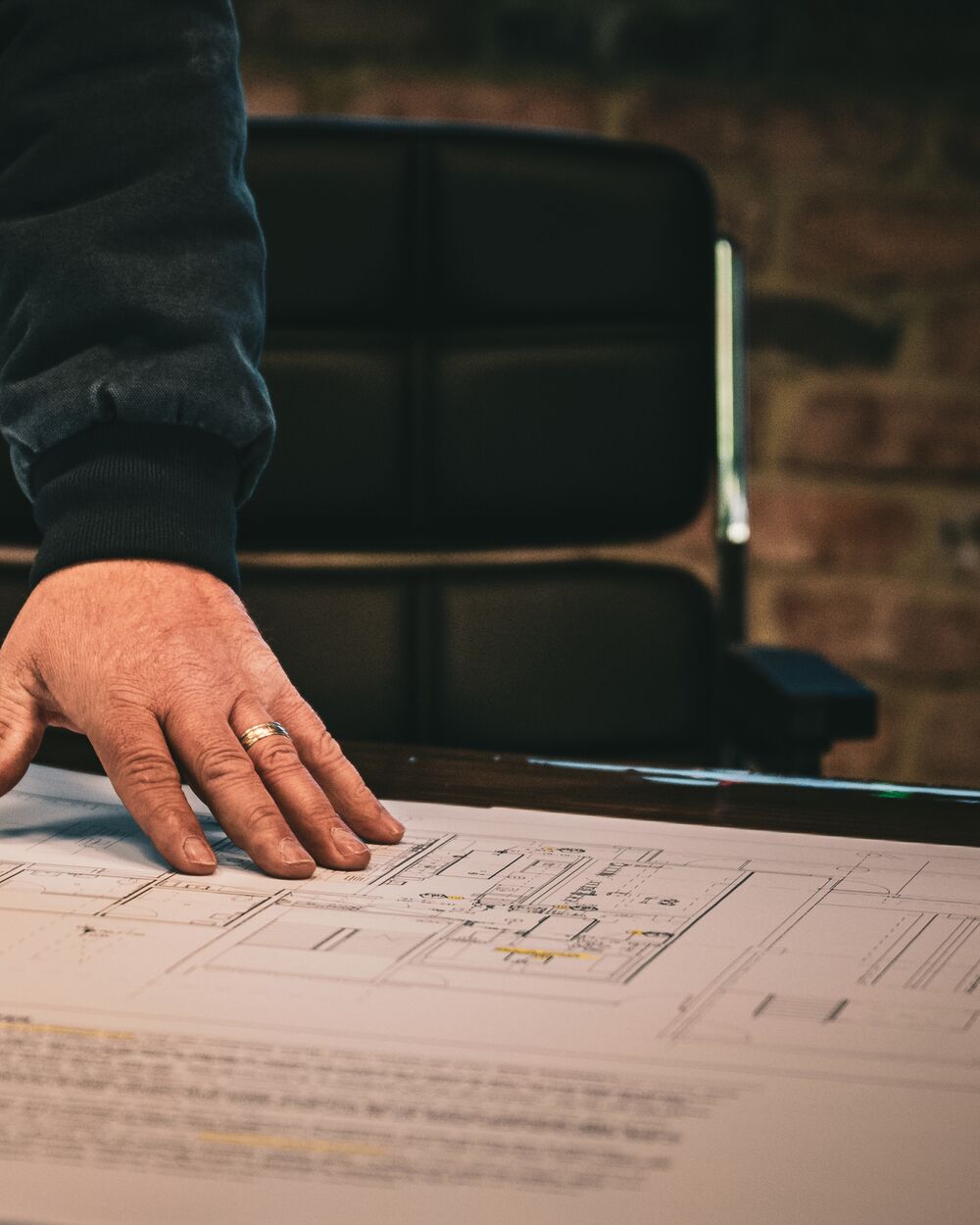 A hand resting on a set of construction drawings spread across a conference table